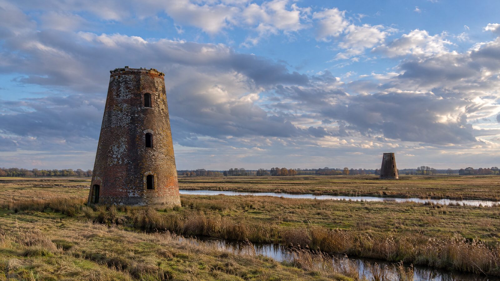 Two derelict brick drainage mills standing on Broadland grazing marsh in autumn